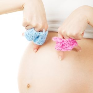Mujer embarazada sujetando pantaloncitos de lana rosa y azul