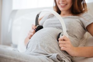Mujer embarazada poniendo auriculares sobre su barriga para transmitirle la música al bebé