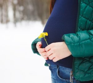 Detalle de tripa de mujer embarazada con jersey y chaqueta en un lugar nevado