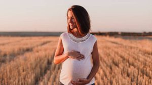 Mujer embarazada en el campo sonriendo y sujetando su tripa